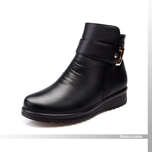 Black ankle boot with gold buckle on side, displayed on a white background with a logo at bottom right.