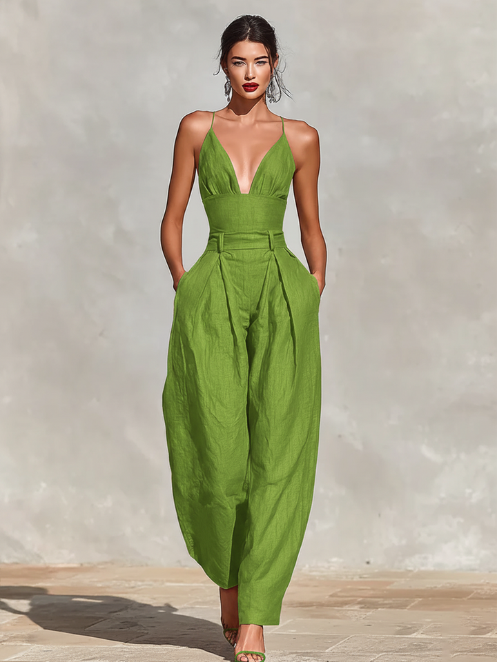 Woman in green, sleeveless jumpsuit with V-neckline and wide legs, on sunlit stone surface.