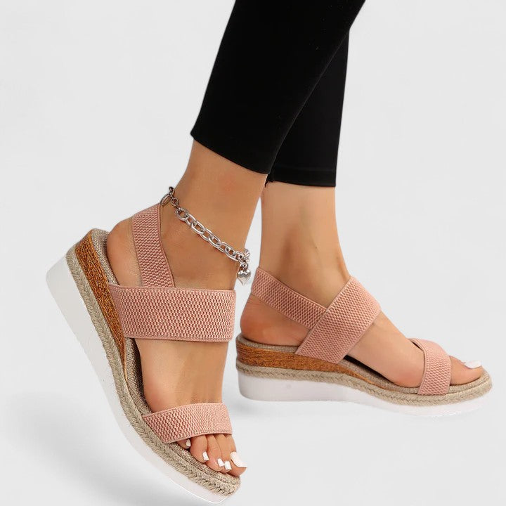 Pink orthopedic sandals with strap design and wedge soles, worn with black leggings and a silver anklet in a studio setting.