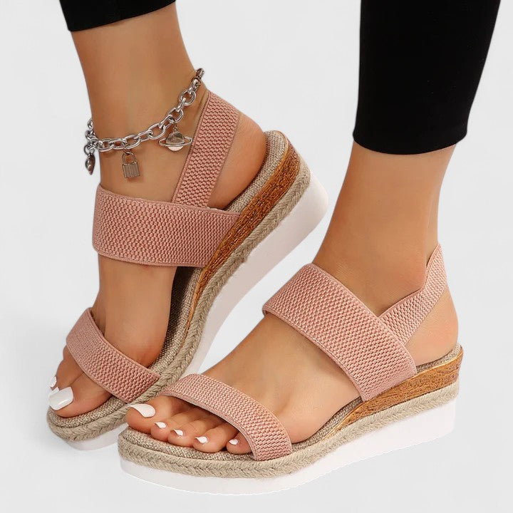 Pink orthopedic sandals with secure straps and platform heels, worn with black leggings and a silver charm anklet in a studio.