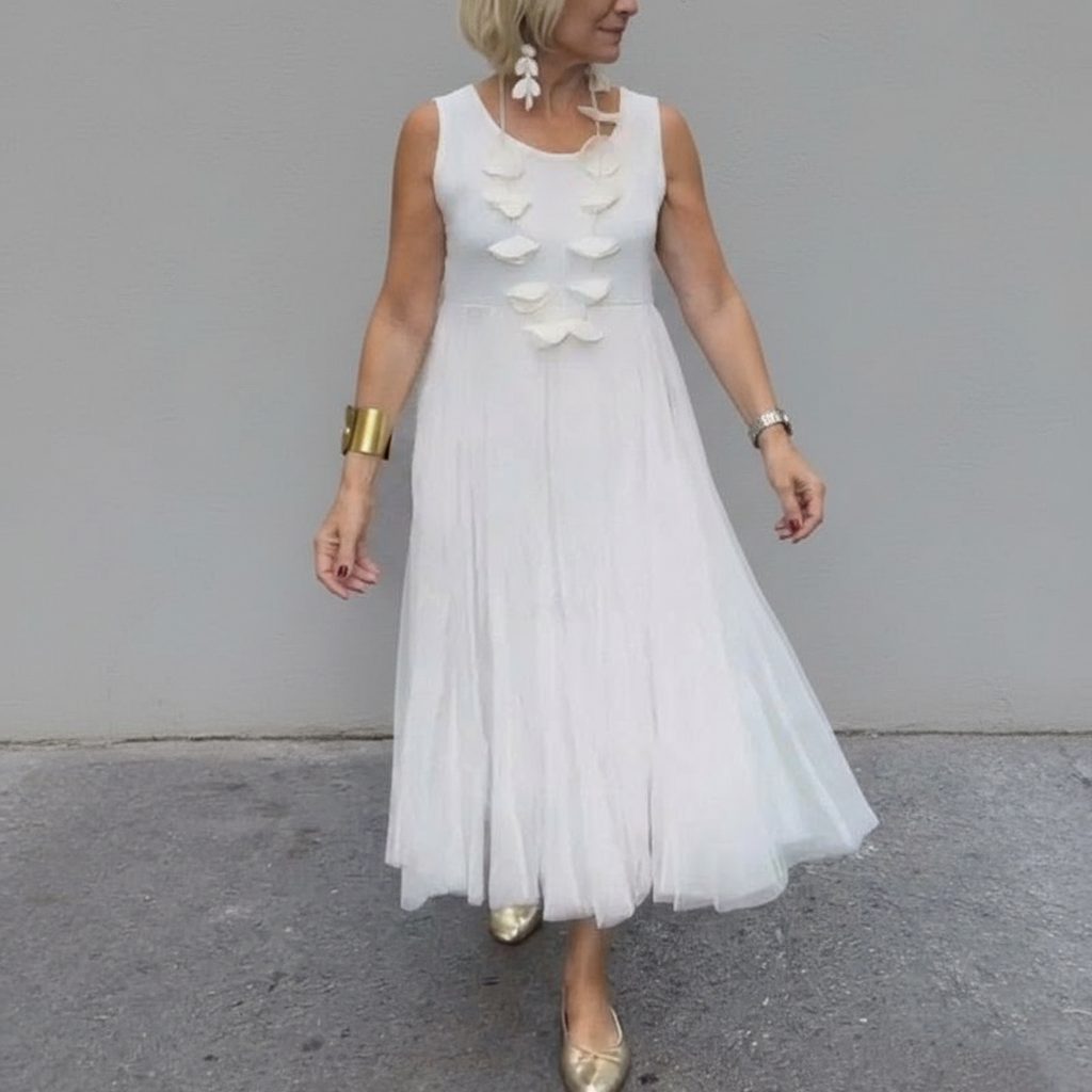 Stylish woman in white sleeveless pleated dress with decorative details, outdoor setting.