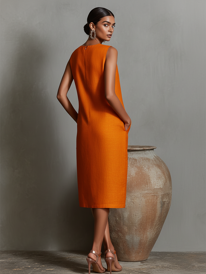 Back view of orange midi dress with pockets, sleeveless, model in studio next to large pottery.