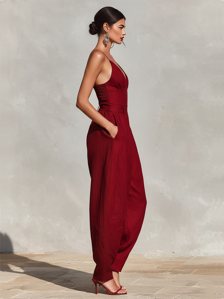 Side profile of woman in deep red jumpsuit with V-neckline, on a stone surface with light background.