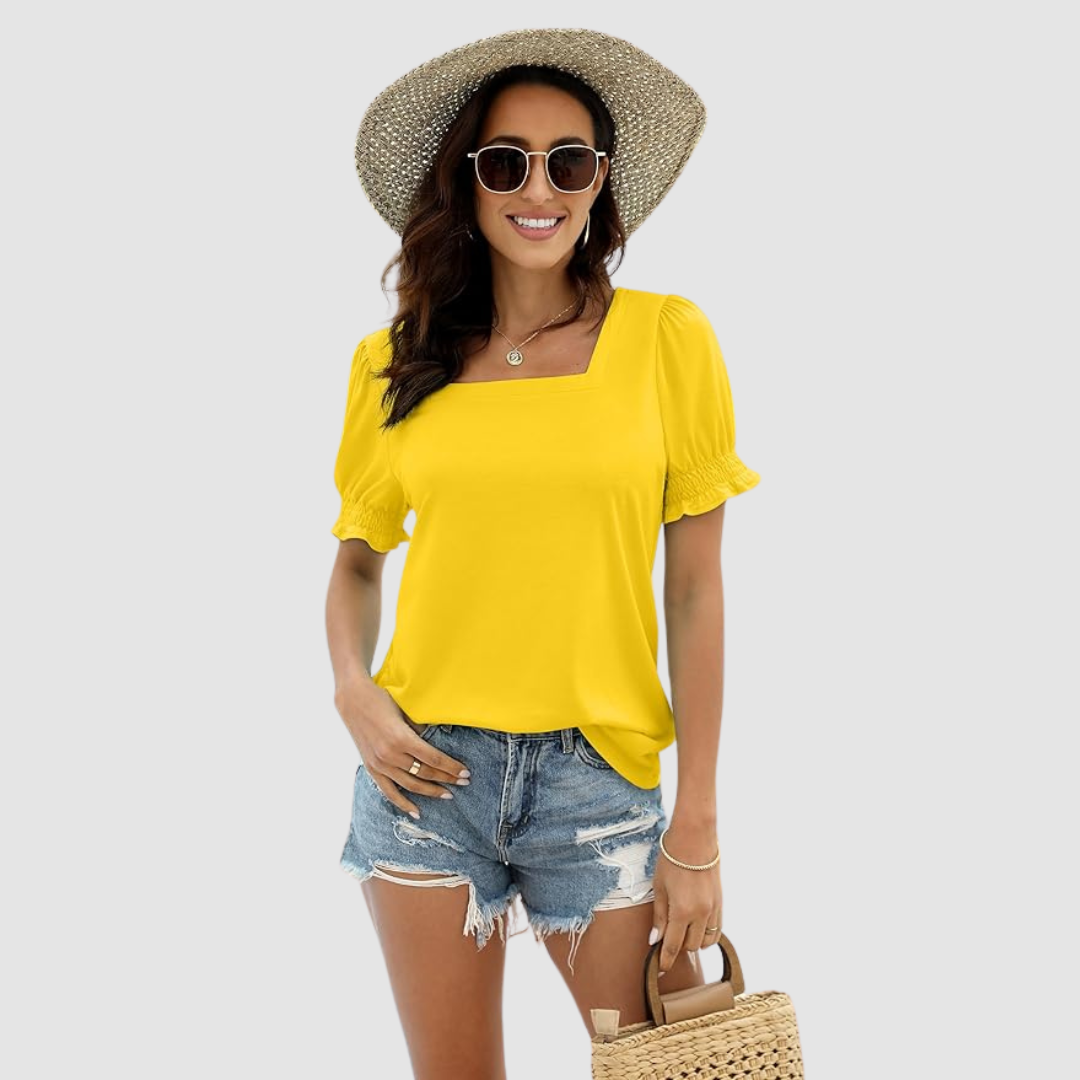 Model in yellow square neck top with puffed sleeves, denim shorts, straw hat, sunglasses against studio backdrop.