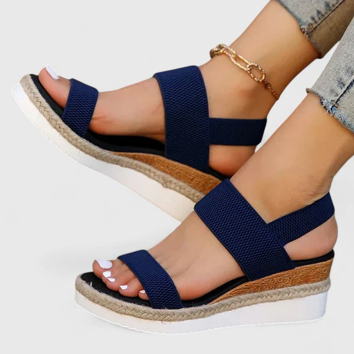 Navy orthopedic sandals with adjustable straps and wedge soles, paired with light denim and a gold anklet in a studio setting.